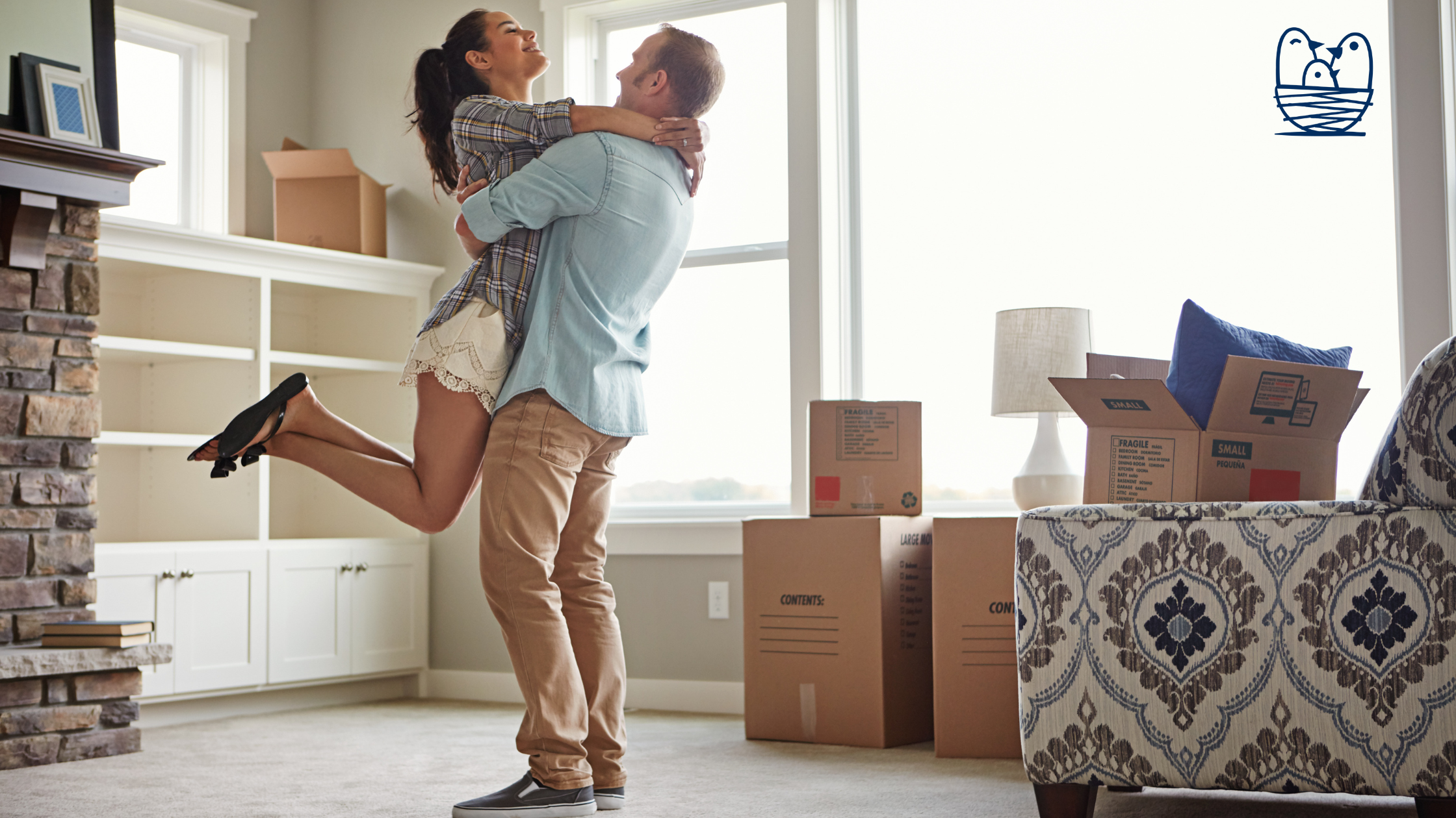 A man holding a woman in a room with unpacked boxes, a window, and some furniture in the background.