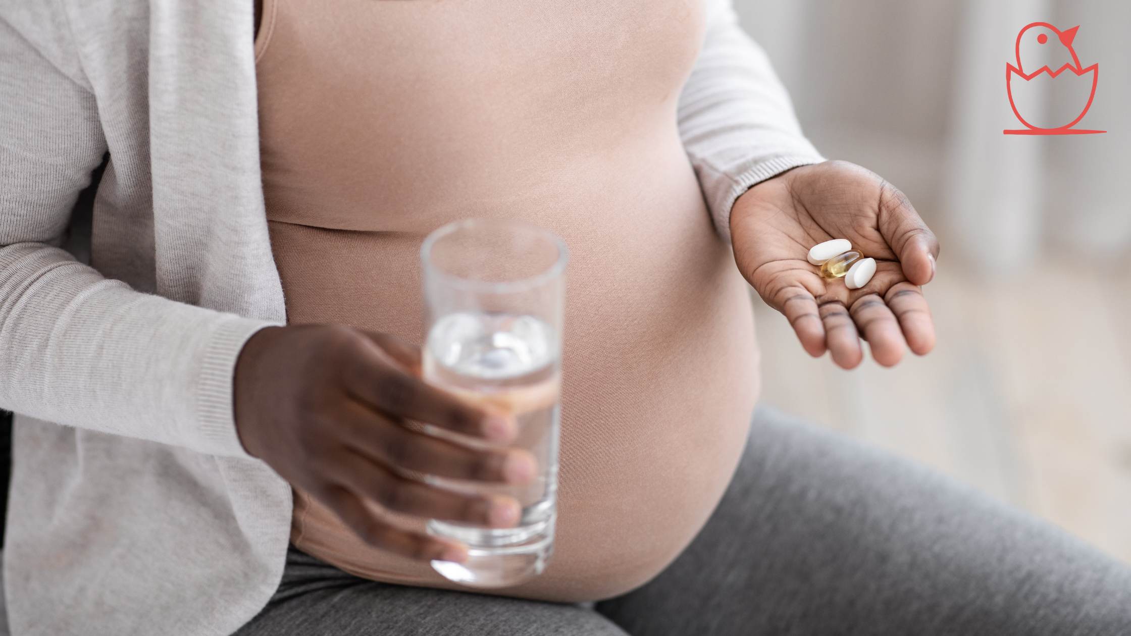 A pregnant woman holding a glass of water and pills.