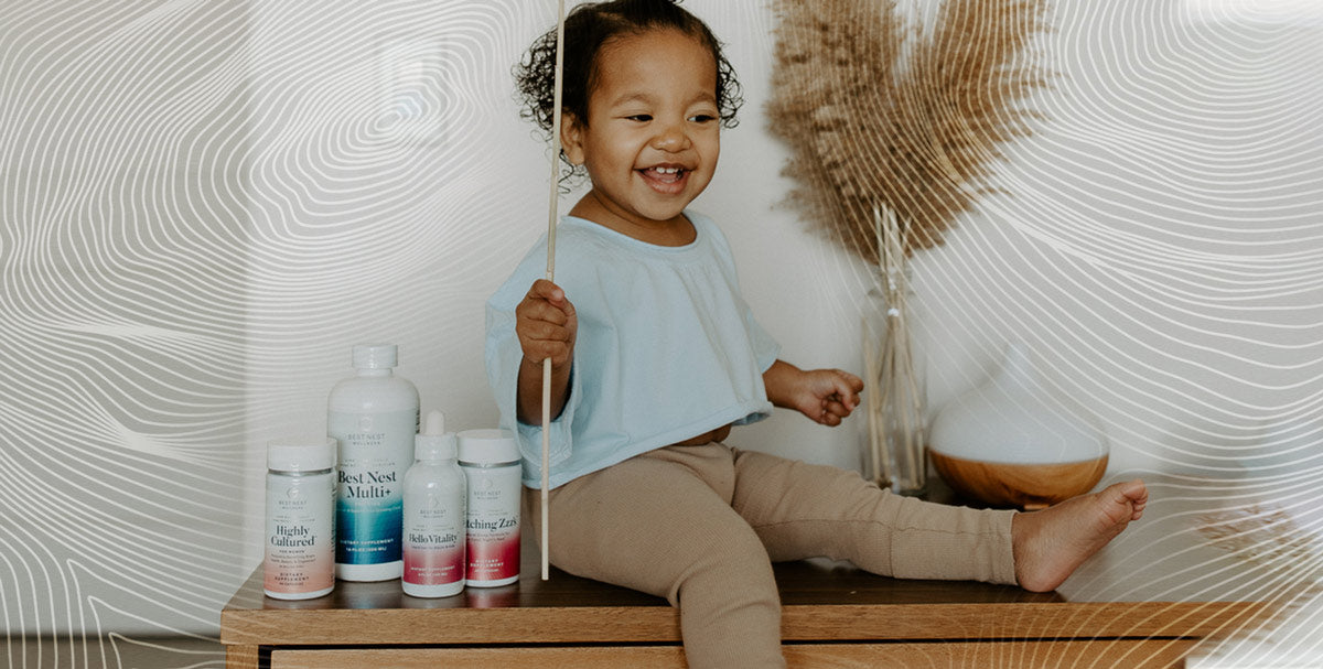 A child sitting on a table, smiling, while holding a stick, with several white bottles visible in the background.