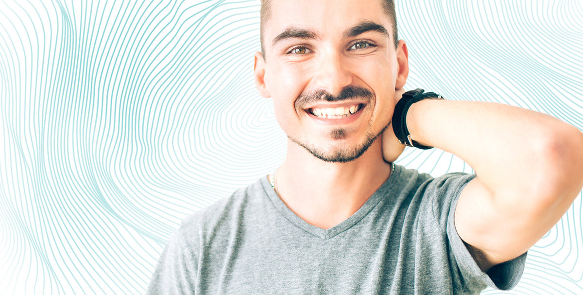A man smiling with his hand on his neck, wearing headphones, close-up on his face and neck, showing teeth.