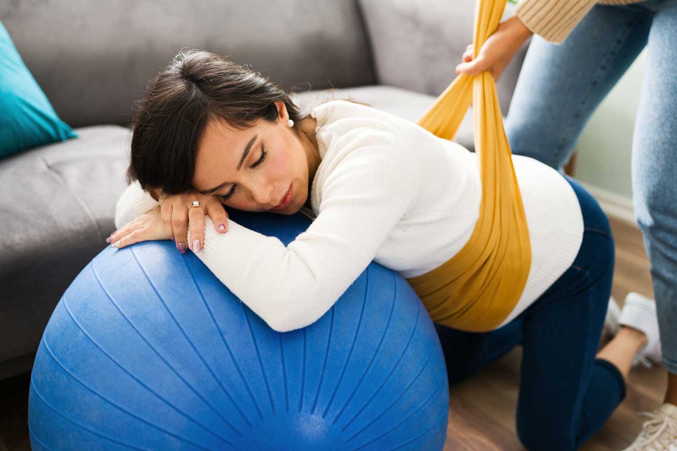 A woman lying on a large blue exercise ball with a yellow band, appearing relaxed.