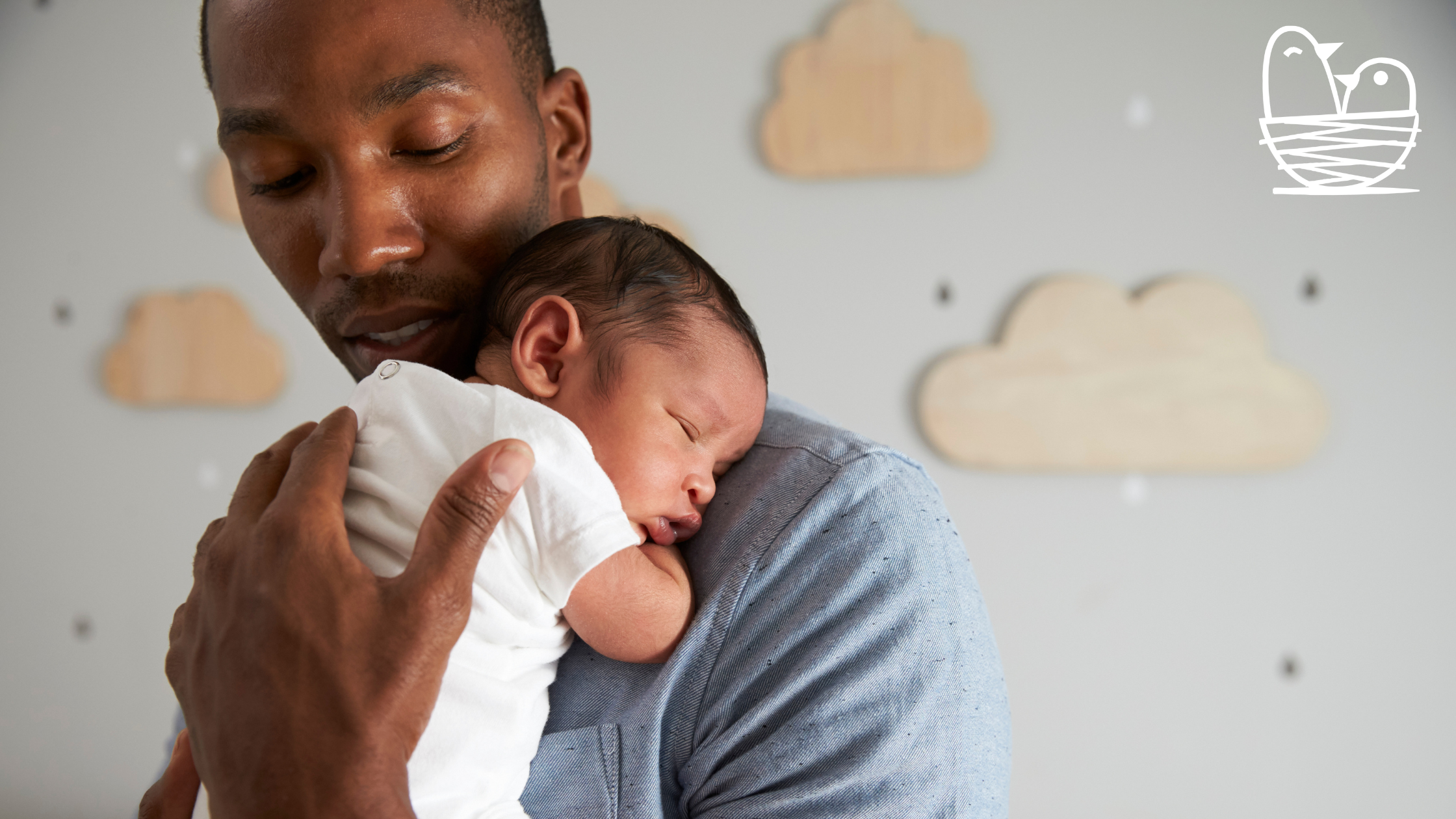A man cradling a sleeping baby on his chest, both appearing content and relaxed in an indoor setting.