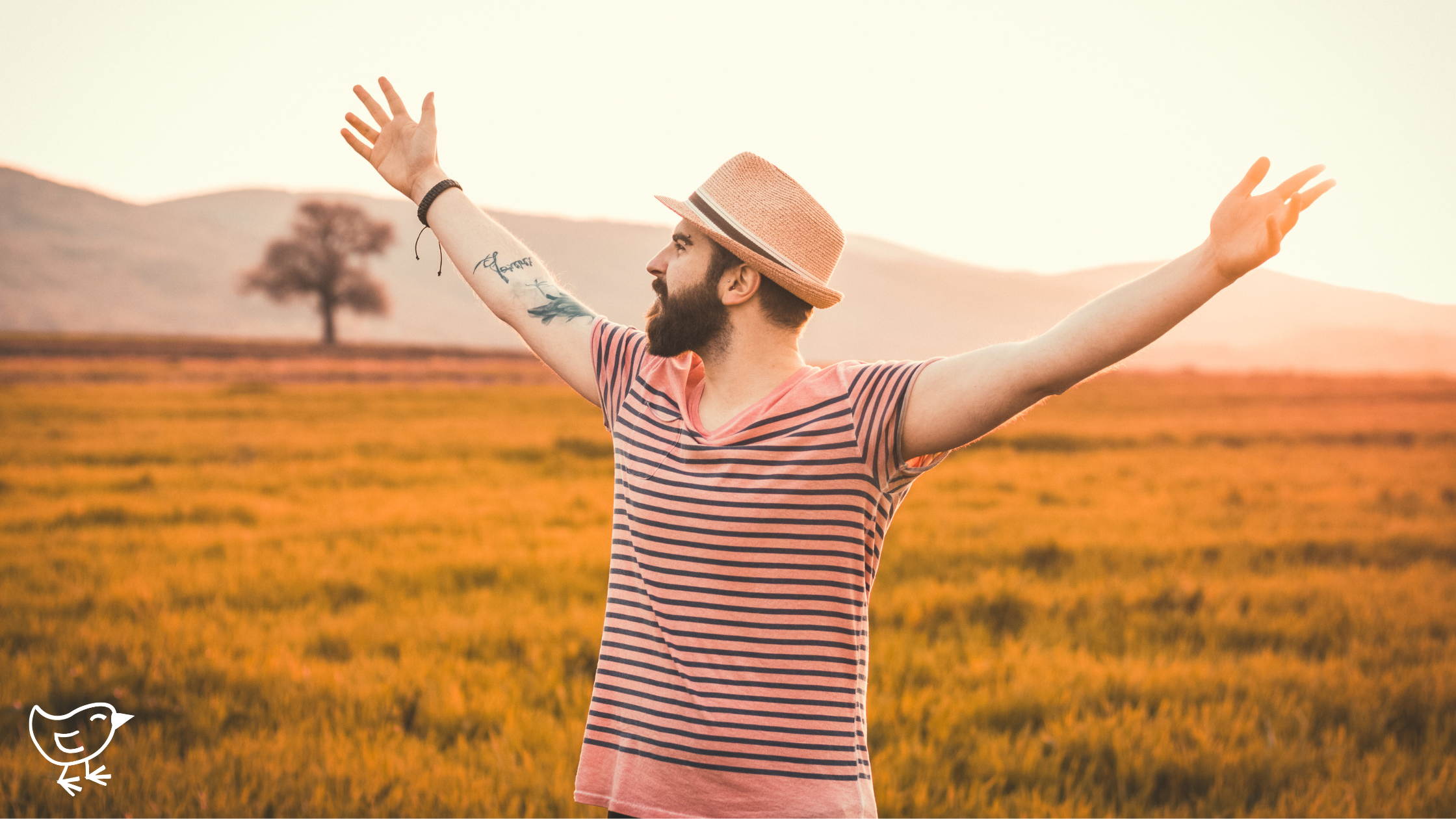 A man with raised arms stands in a grassy field, wearing a hat.