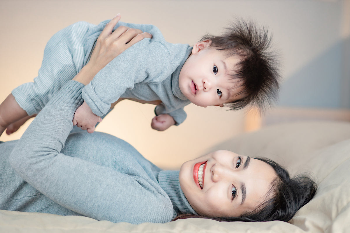 Woman lying on a bed holding a baby above her