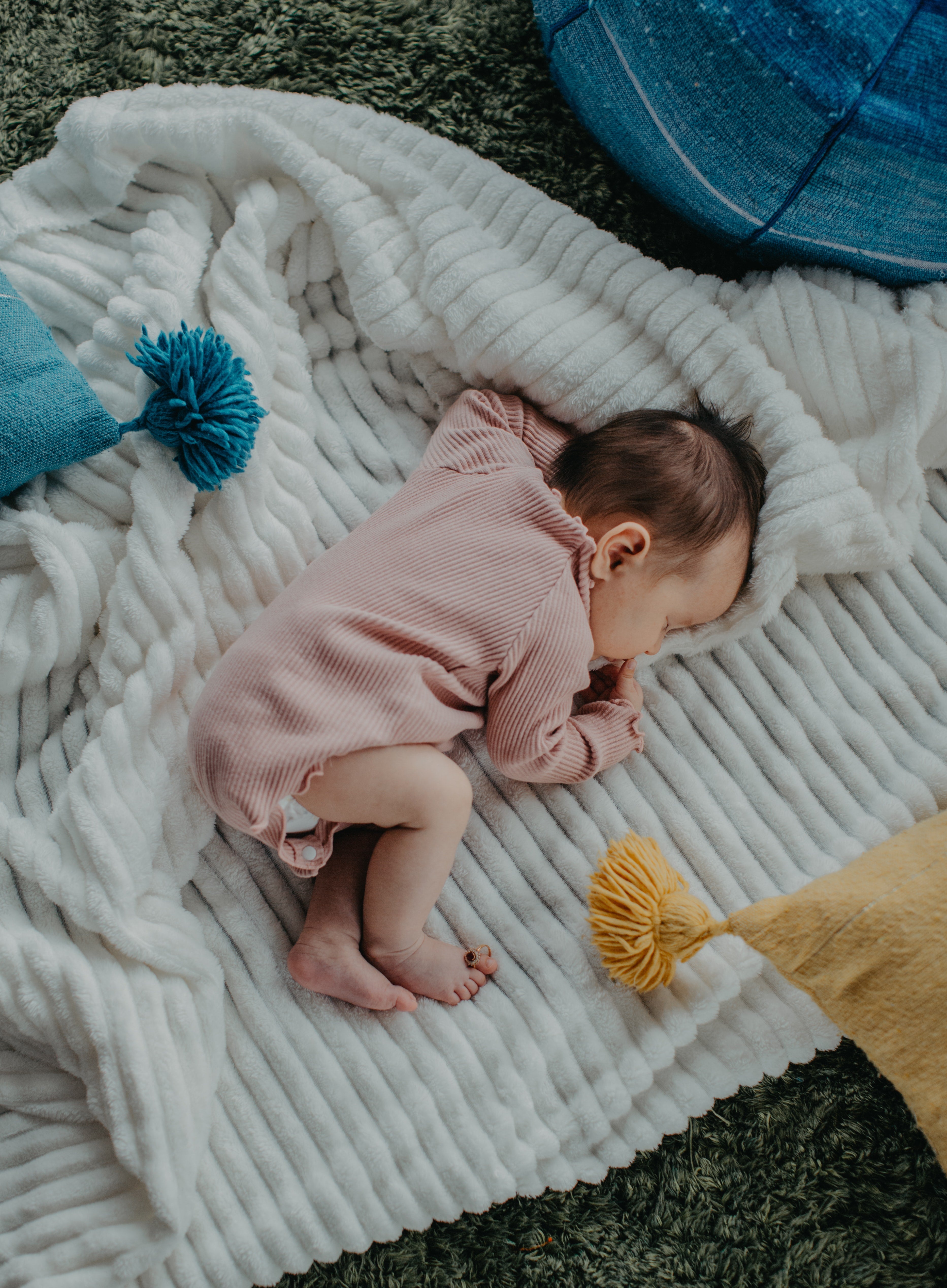 Sleeping baby in white outfit resting peacefully outdoors on soft blanket surrounded by green grass and sunlight